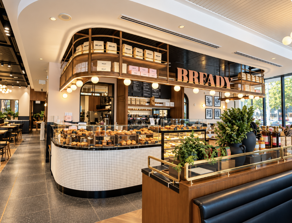 Inside Bready York & Adelaide — curved pastry counter, brass shelving and glowing globe lights